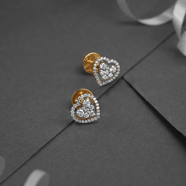Two elegant heart-shaped earrings with gold backs and diamond-studded fronts on a dark gray surface. The scene conveys luxury and sophistication.
