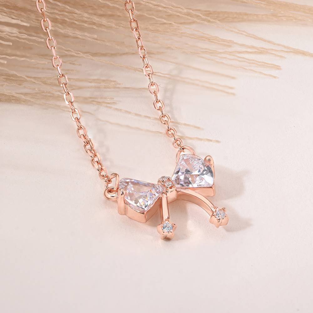 Rose gold necklace with a bow-shaped pendant featuring two triangular and two small circular crystals. Set on a delicate chain, conveying elegance and charm.