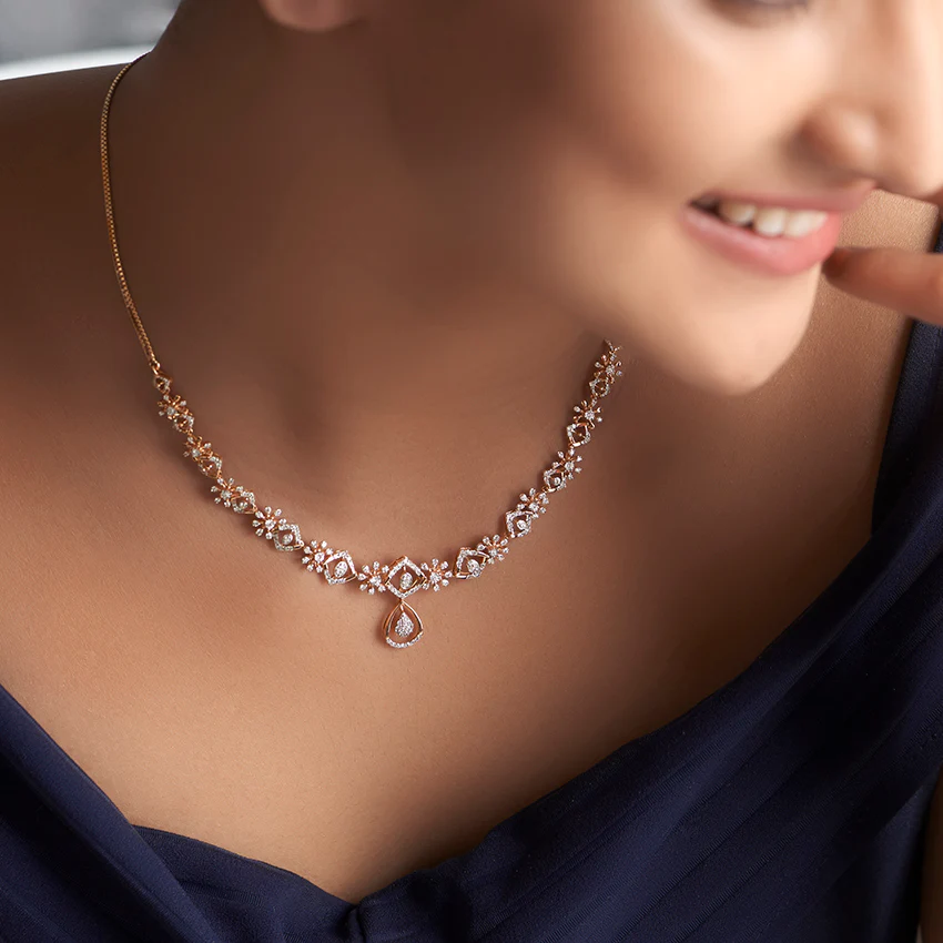 A woman wearing a diamond necklace with intricate floral designs and a teardrop pendant, smiling softly. She is dressed in an elegant navy outfit.